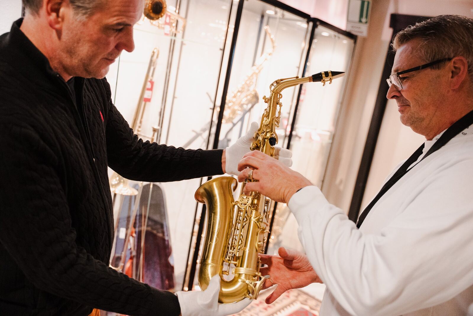 Medewerker overhandigt een saxofoon met witte handschoenen aan een klant
